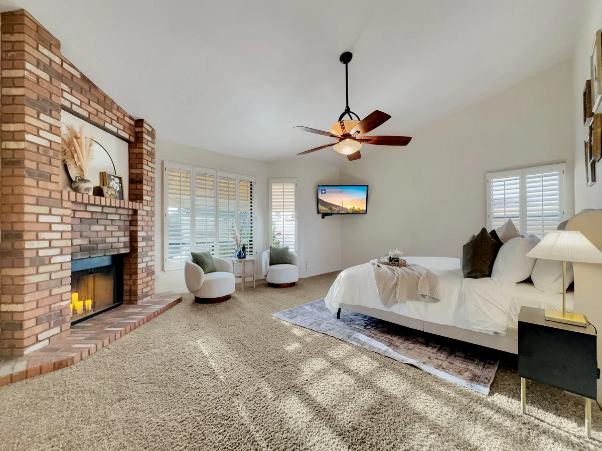 A spacious and inviting bedroom featuring a plush bed, cozy seating area, fireplace, and a wall-mounted television. Natural light streams in, enhancing the calming, restful mood of the suite. The thoughtful layout provides both relaxation and modern amenities.