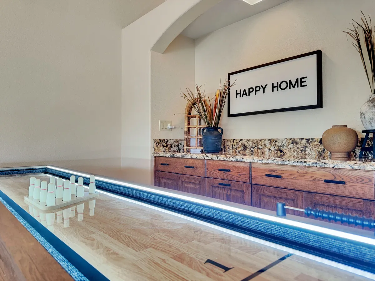 A cheerful interior scene centered around a game table, with a warm, inviting ambiance. The 'HAPPY HOME' sign, decorative accents, and a unique arrangement of bowling pins speak to fun and togetherness, suggesting a space designed for game nights and laughter with family and friends.