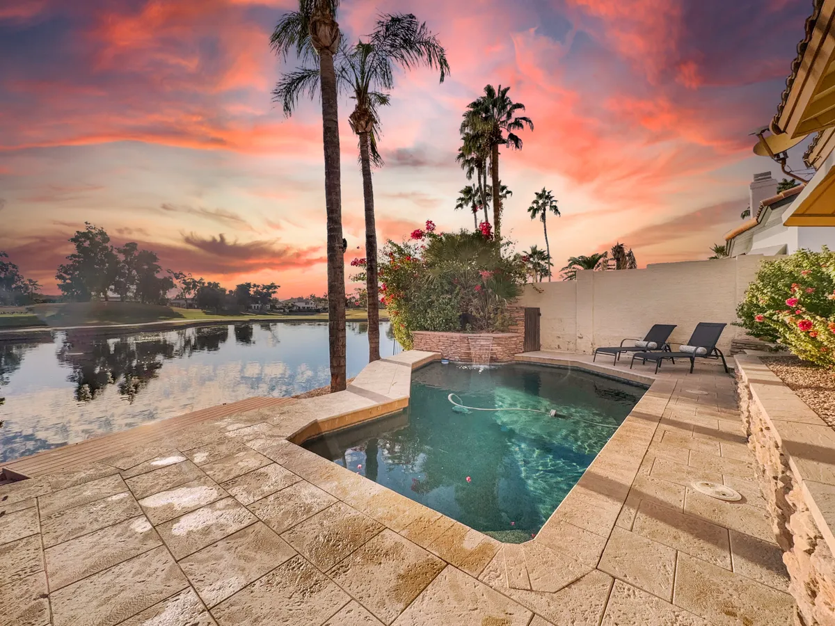 An inviting swimming pool bordered by palm trees, with a vibrant sunset sky reflecting on the tranquil water. The scene suggests opportunities for relaxation and social gatherings in a beautiful, resort-like outdoor setting.