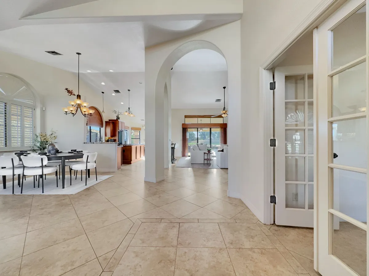An inviting open-plan dining area anchored by a grand table with chairs, seamlessly connected to the kitchen and a cozy living area. Large windows flood the space with natural light, enhancing the sense of openness and warmth ideal for gatherings.