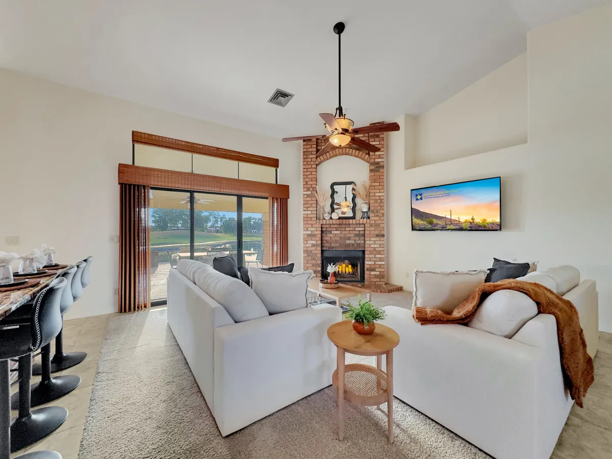A welcoming space featuring a stylish fireplace, large windows bathing the room in light, comfortable sofas, a television, and a visible dining area. The ambiance is cozy, ideal for winding down an evening by the fire.