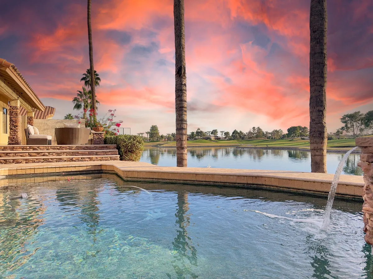A sparkling swimming pool bordered by palm trees and lush landscaping, with a stunning sunset sky reflecting on the water. The area is ideal for relaxing, entertaining, or enjoying a peaceful evening outdoors.