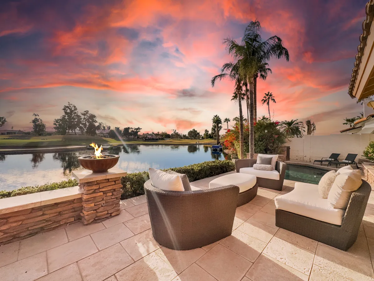A cozy outdoor seating space with a fire pit, surrounded by palm trees and overlooking the tranquil lake at sunset. The scene invites intimate conversations and showcases the potential for outdoor relaxation.