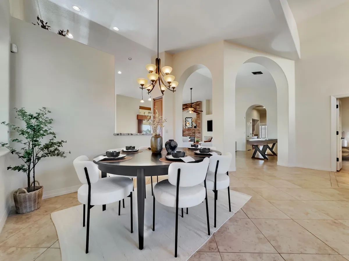 A warmly lit dining room with a stylish table, chandelier, arched doorways, and a potted plant, fostering a welcoming vibe for entertaining guests or celebrating special occasions.