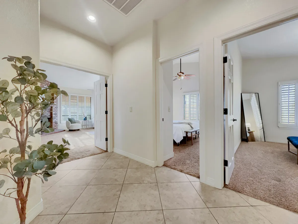 An interior scene showing doorways leading to different rooms, including a visible bedroom setup, living area, and decorative details like a potted plant and mirror. This view suggests connectivity and flexible use of space.